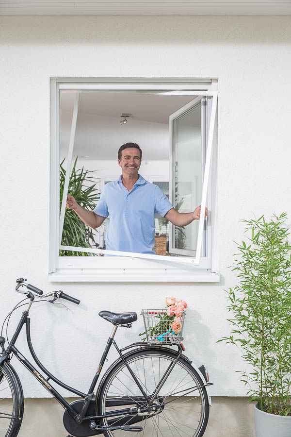 Mann hält passgenaues Fliegengitter am Fenster – Insektenschutz nach Maß aus Weißenhorn